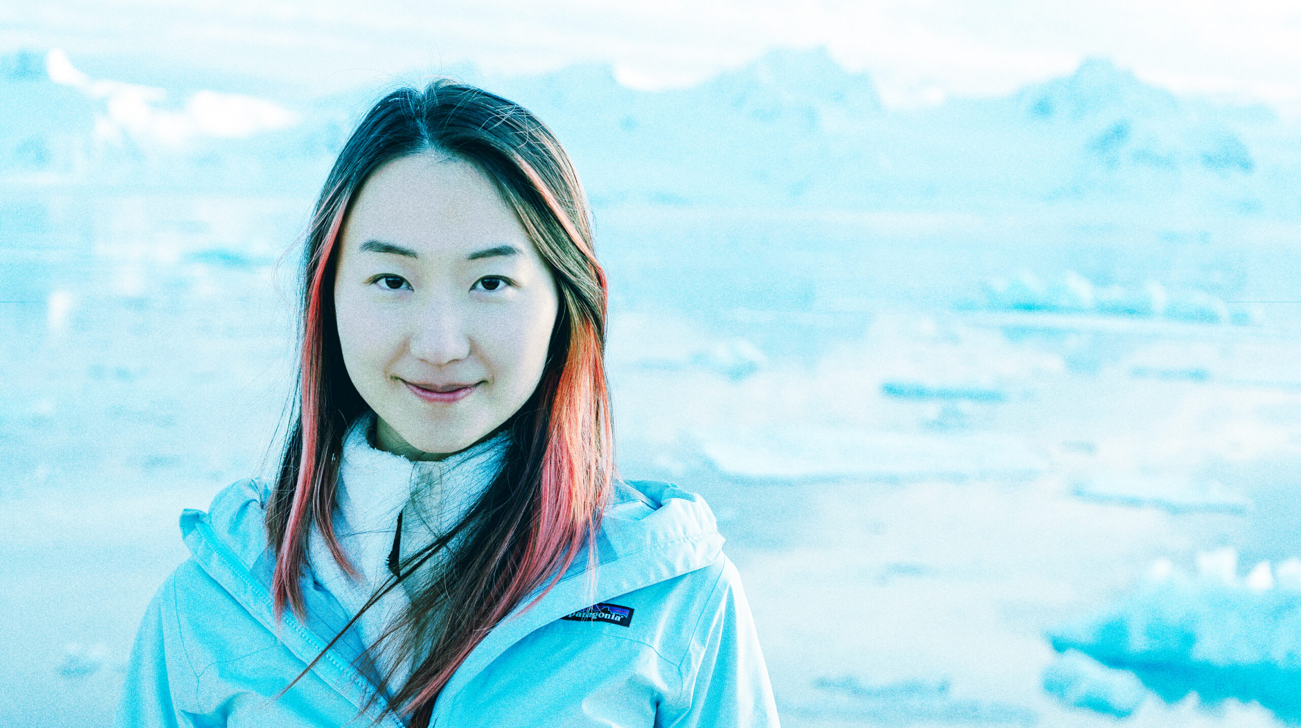 iabao Li in a white parka smiling with icebergs in the background.