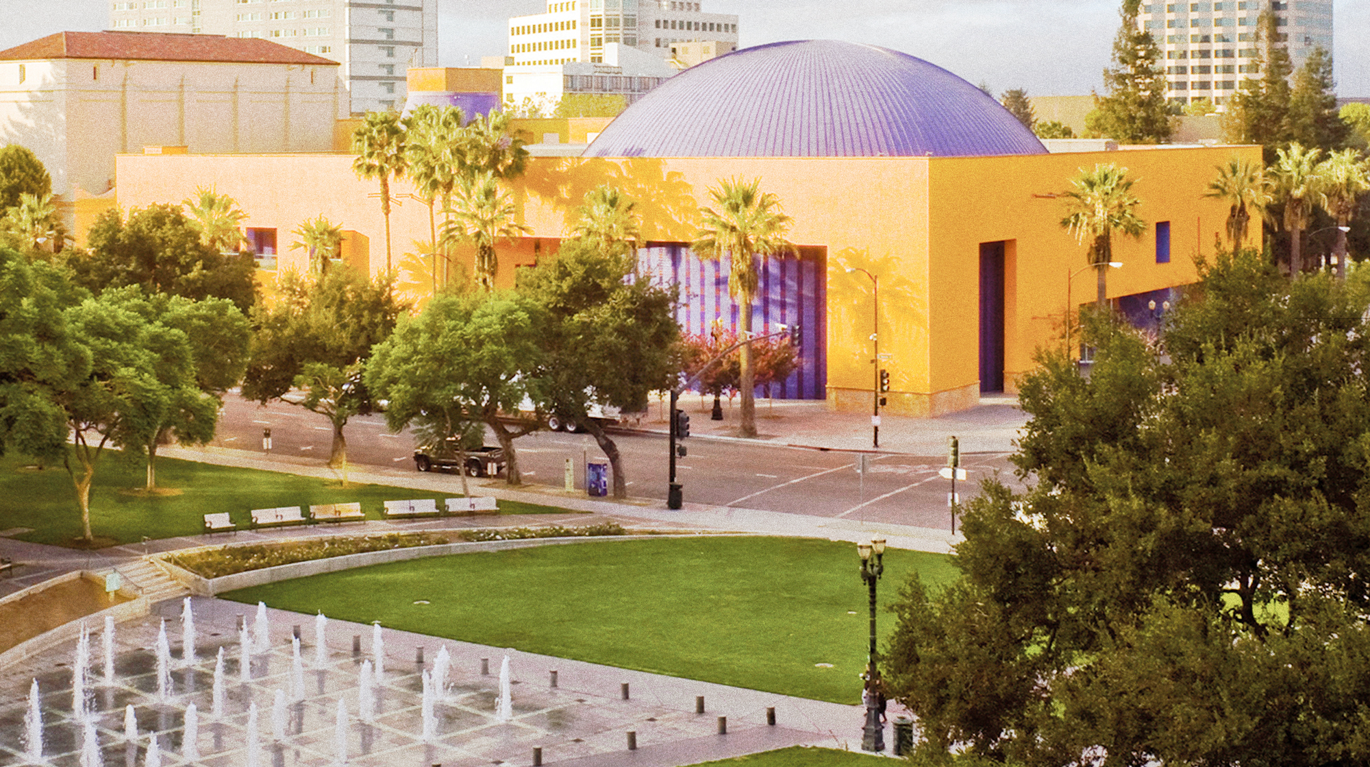 Photo of the orange-colored The Tech Interactive, with its domed roof, viewed from nearby Plaza de César Chávez in Downtown San Jose