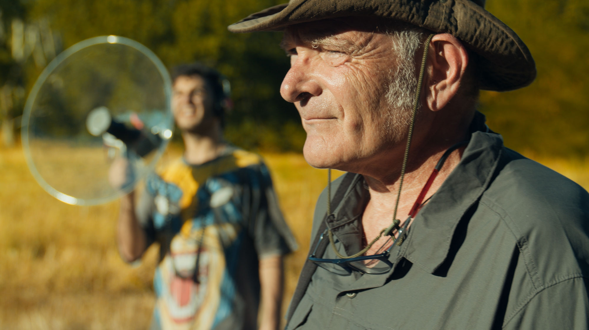 Man with hat standing in front of a man holding a bird and an antenna.